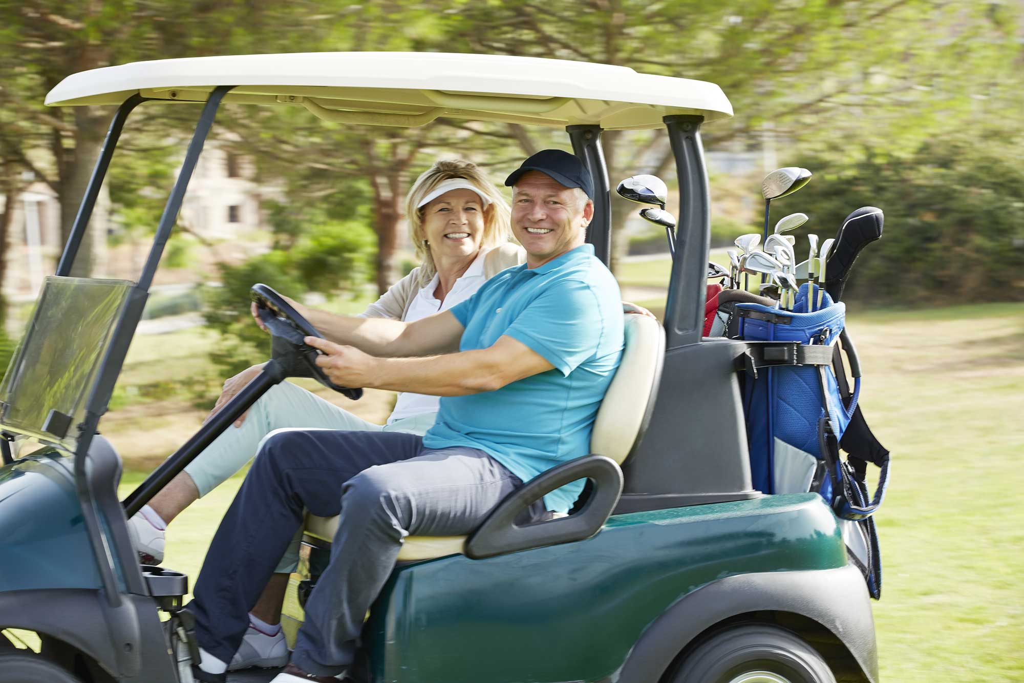 Happy senior couple riding in a golf cart at the golf course.